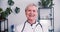 Happy beautiful senior Caucasian female doctor wearing lab coat and stethoscope smiles at camera sitting at light office