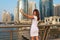 Happy beautiful tourist woman in fashionable summer white dress and sunglasses shooting mobile phone in Dubai marina in United