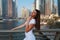 Happy beautiful tourist woman in fashionable summer white dress walking and enjoying in Dubai marina in United Arab Emirates.