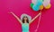 Happy beautiful woman with bunch of colorful balloons raising her hands up on pink background