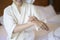 Happy beautiful woman in white bathrobe applying body moisturizing cream in bedroom, skin care and treatment concept