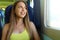 Happy beautiful young woman looking through the train or bus window. Smiling pretty train passenger traveling sitting in a seat