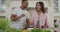 Happy biracial man feeding woman with vegetables in kitchen