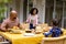 Happy biracial parents and daughter serving food and sitting at table for meal on terrace