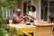 Happy biracial parents and daughter serving food and sitting at table for meal on terrace