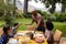 Happy biracial parents, son and daughter serving food and sitting at table for meal in garden