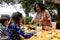 Happy biracial parents, son and daughter serving food and sitting at table for meal in garden