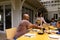 Happy biracial parents, son and daughter serving food and sitting at table for meal on terrace