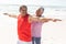 Happy biracial senior woman helping man practice yoga with arms outstretched at sunny beach