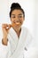 Happy biracial woman in bathrobe brushing teeth in sunny bathroom