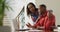 Happy biracial woman with coffee embracing partner sitting at desk with laptop and paying bills