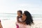 Happy biracial woman giving piggyback ride to daughter at beach against sky with copy space