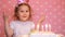 Happy birthday. Cute child make a wish and blows out candles on cake at party. Funny little girl. pink background