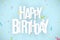 Happy birthday inscription. White paper chaotic letters on a light blue background. Explosion of multicolored confetti. Festive gr