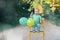 Happy birthday. Smiling little child boy in paper crown with balloons sitting on chair outdoor. Cute toddler celebrating birthday