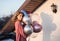 Happy birthday teenage girl in pink dress holding a bunch of colorful balloons, stands near house on a sunny day