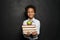 Happy black child student holding books and apple and smiling on chalkboard background