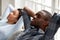 Happy black couple relax on couch hands over head