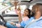 Happy black couple sitting in car pushing buttons