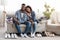 Happy Black Couple Sitting On Couch With Folded Clothes And Shoes Around