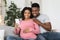 Happy black expecting couple taking selfie at home, using phone