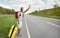 Happy black guy with backpack and suitcase flagging down car, needing ride, hitchhiking on roadside, copy space