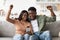 Happy black lovers using smartphone together and gesturing, home interior