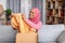 Happy black muslim woman opening carton box, checking her delivery, holding new clothes and smiling