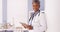 Happy Black Senior doctor standing in office with tablet