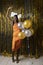 Happy black woman in formal dress have fun with raised arms in festive hall with gold decorations and colored balloons