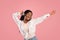 Happy black woman in headset dancing to beautiful music on pink studio background