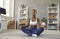Happy black woman sitting on floor at home, practicing yoga, relaxing and meditating