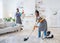 Happy black woman vacuuming floor while her boyfriend dusting cushion at their apartment, copy space