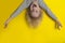 Happy blond boy hanging upside down with arms outstretched. Portrait of child on bright yellow background