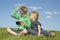 Happy blond children using smartphone (watching movie or playing game) sitting on the grass.