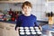 Happy blond school kid boy baking blueberry vanilla muffins in domestic kitchen, indoors. Funny lovely healthy child