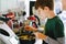 Happy blond school kid boy baking plum cake in domestic kitchen, indoors. Funny lovely healthy preteen child having fun