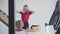 Happy blond woman walking down the stairs and joining daughter sitting at the table. Sleepy Caucasian mother stretching