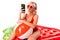 Happy blonde caucasian female stands in swimsuit with big rubber mattress, phone, earphones, do selfie and smiles
