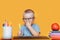 Happy blonde clever boy is sitting at a desk in glasses and smiling. Ready for school. Back to school. Apple, pens and books on