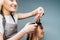 Happy blonde female barber trimming client`s hair over blue background