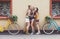 Happy boho chic girls pose with bicycles near house facade