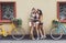 Happy boho chic girls pose with bicycles near house facade