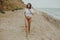 Happy boho girl in white shirt running on sunny beach. Carefree stylish woman in swimsuit and shirt relaxing on seashore. Summer