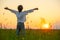 Happy boy with raised hands looks at the sunset  in summer. Boy in a field with his hands raised while sunrise. Freedom and