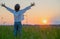 Happy boy with raised hands looks at the sunset  in summer. Boy in a field with his hands raised while sunrise. Freedom and