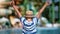 Happy boy rejoicing raising hands at resort with water slides. Shot on RED Raven 4k Cinema Camera