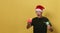 A happy boy in a Santa hat and a green T-shirt is holding a gift against a blue background
