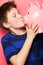 Happy boy, savings and kiss on piggy bank for investment, money or coins against a pink background. Little child or kid