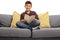 Happy boy seated on sofa holding a book and looking at camera